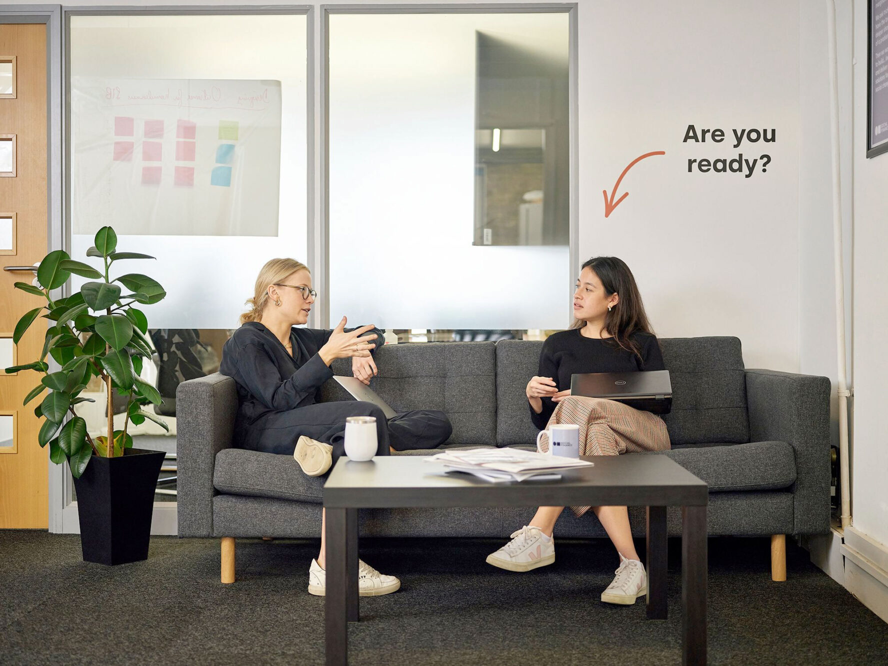 Two people sitting on a sofa talking. Behind them is a slogan reading 'Are you ready?'