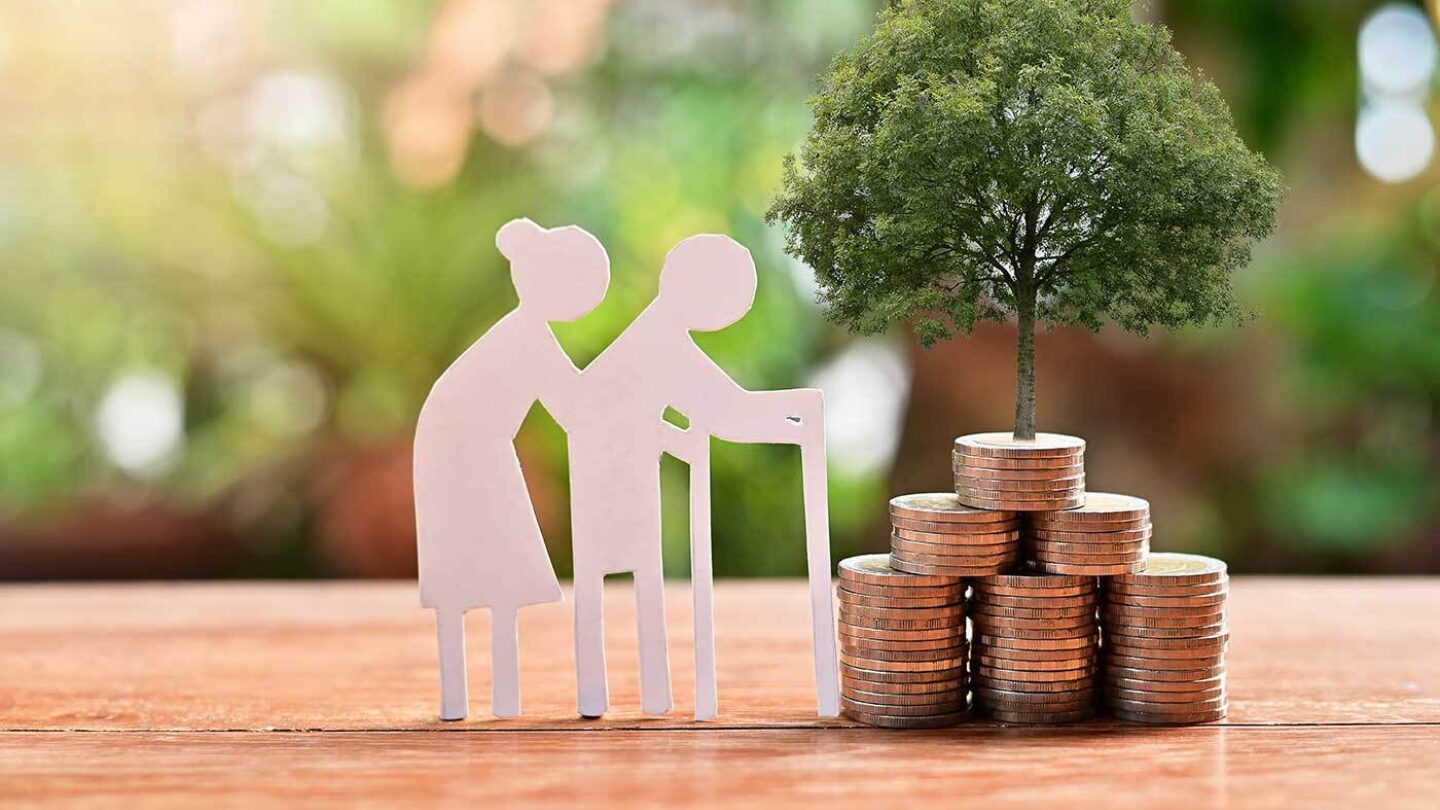 A cardboard cutout of an older couple besides a pile of coins. A small tree is sprouting from the top of the coins.