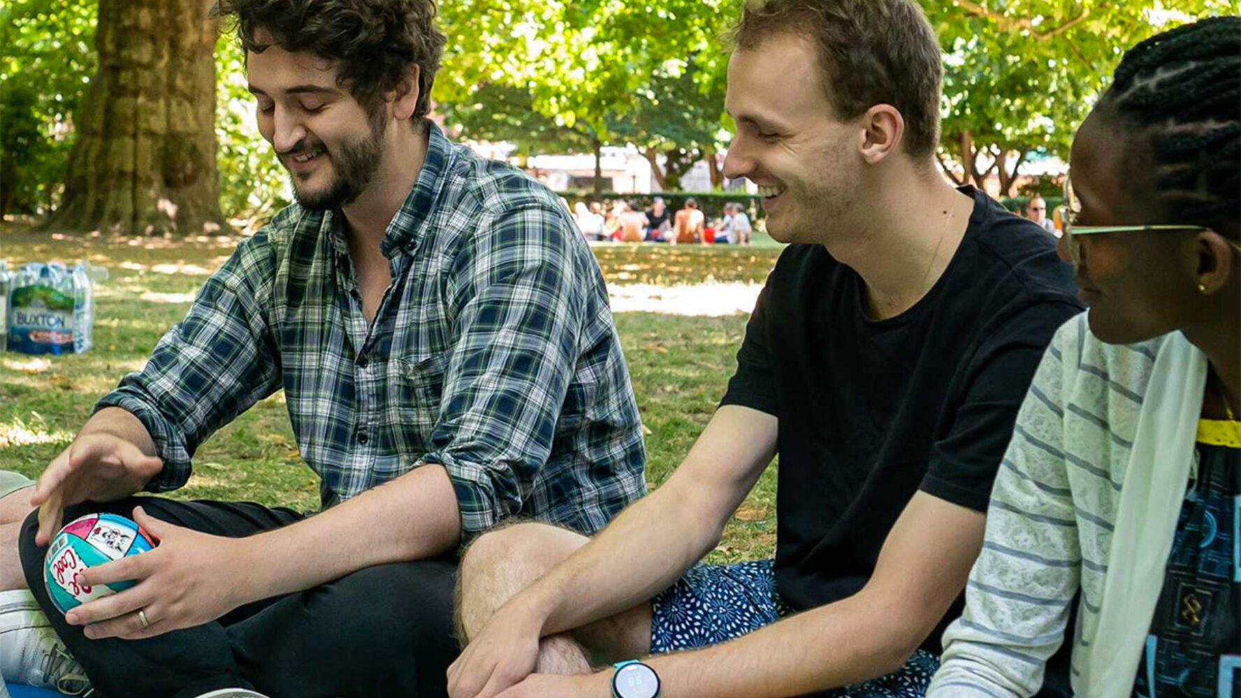 Three people sitting at a picnic in a sunny park, they are smiling.
